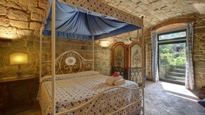 A four-poster bed with a canopy, a stone wall, a wooden cabinet with floral paintings, and a window with curtains. - Villa Chiara - Homelike Villas (Greve in Chianti)