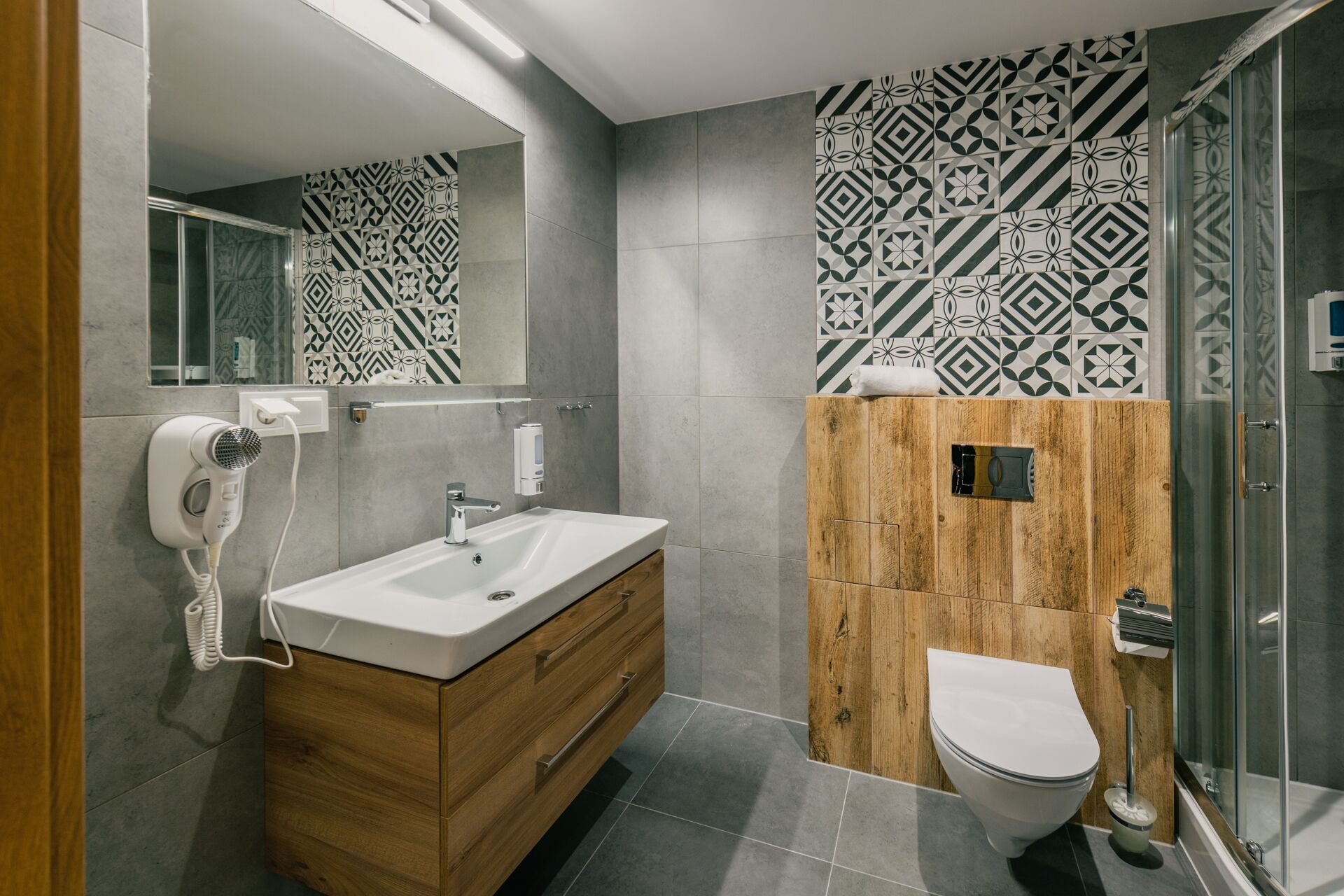 A modern bathroom with a wooden vanity, a white sink, a toilet, and a shower area.