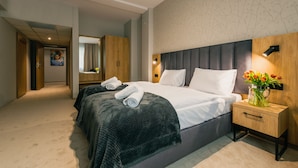 Habitación de hotel moderna con una cama grande, un armario de madera, una mesita de noche con un florero y un espejo sobre la cama.
