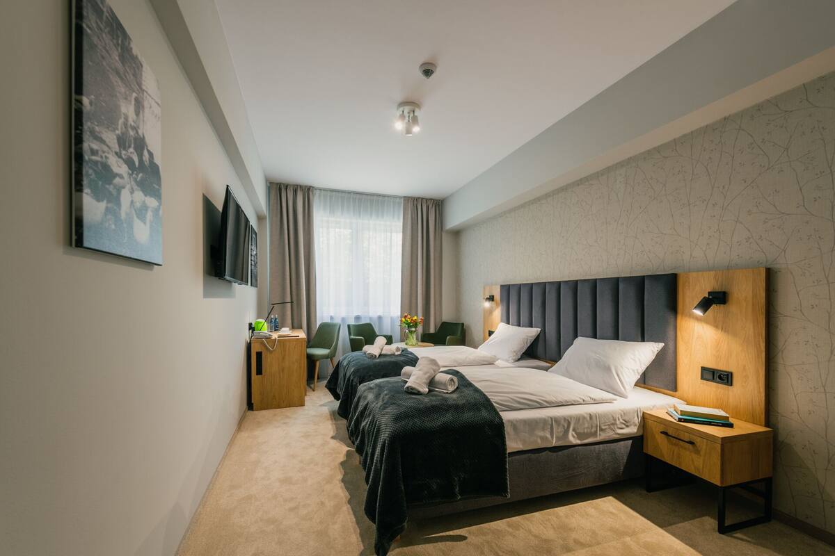 A modern hotel room with a large bed, a desk, a chair, and a TV.