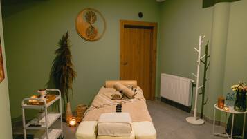 Relax in a serene spa room with a neatly made bed, massage table, and calming green walls.