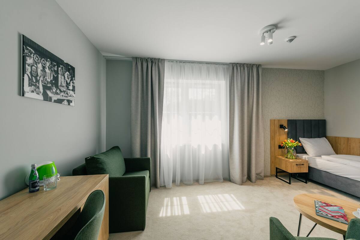 A modern hotel room with a bed, a desk, a chair, a small table, and a nightstand.
