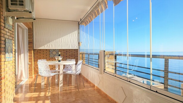 A balcony with a table and chairs, a bottle of wine, and a view of the sea.
