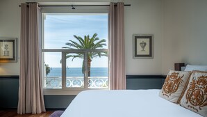A hotel room with a large bed, a view of the sea, and a balcony with a palm tree. - La Villa Mauresque (Saint-Raphaël)