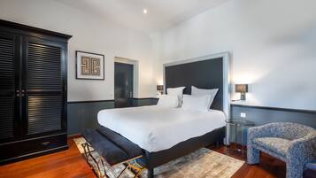 A modern bedroom with a large bed, a dark wooden wardrobe, a small round table, and a patterned armchair.