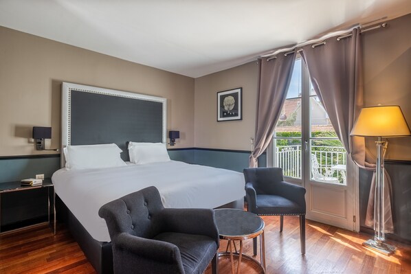 A hotel room with a large bed, two bedside tables, a chair, a small table, and a window with curtains.