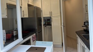 Una cocina moderna con armarios blancos, un refrigerador de acero inoxidable, una encimera con una computadora portátil y un fregadero.