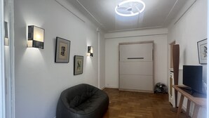 Un pasillo con un sillón de cuero negro, obras de arte enmarcadas en las paredes y piso de madera.