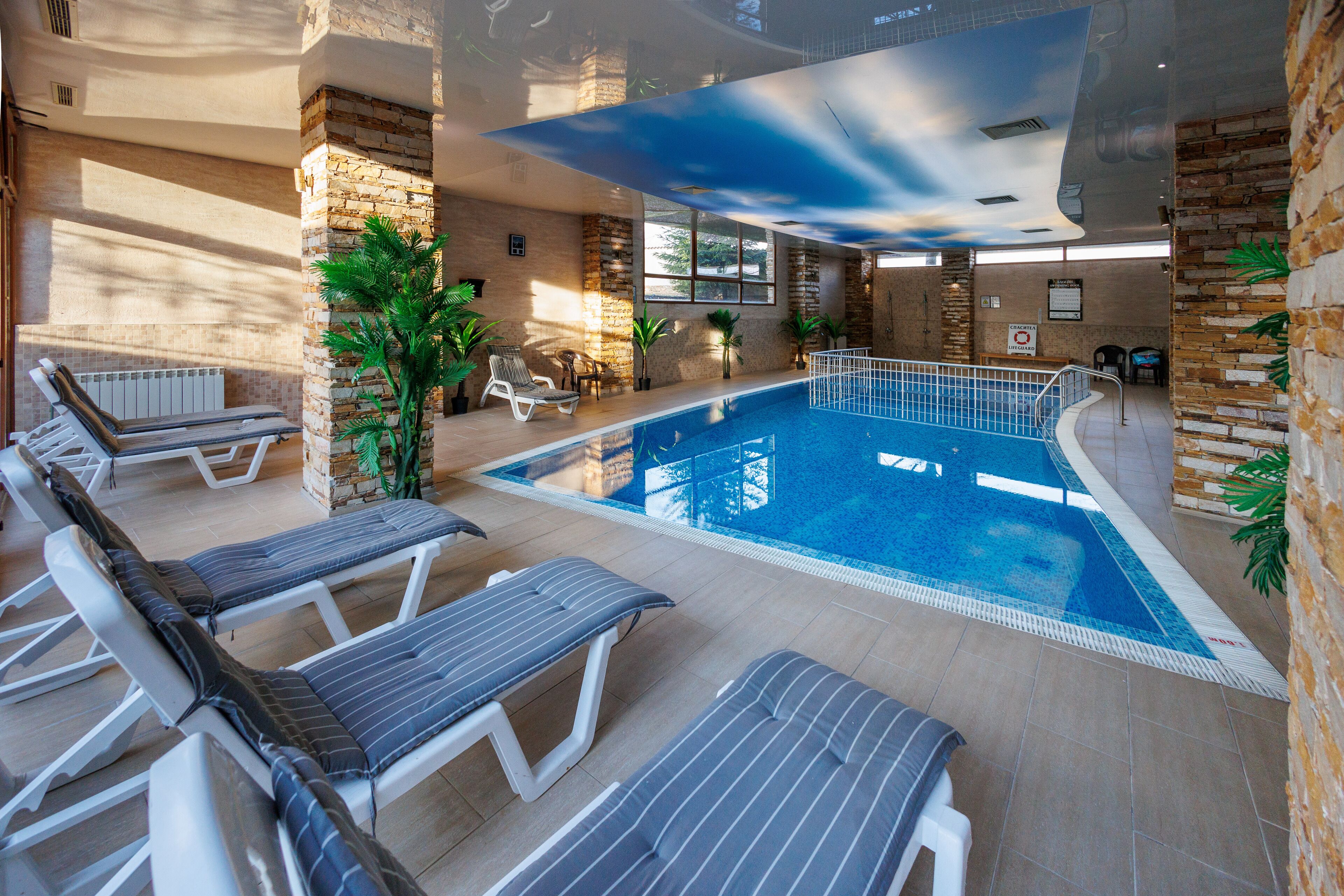 An indoor swimming pool with lounge chairs, potted plants, and stone walls.