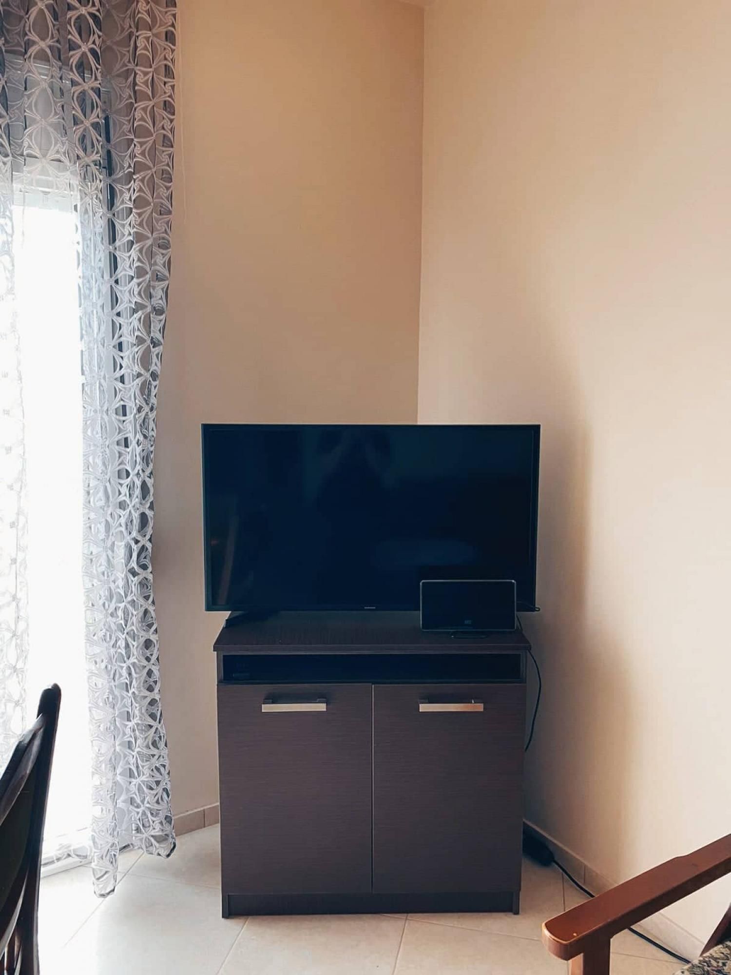 En moderne stue med et fladskærms-tv på et mørkt træskab, en bærbar computer ovenpå og en stribet gardin ved vinduet.