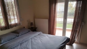 Een slaapkamer met een bed, een nachtkastje, een lamp en uitzicht op de buitenwereld door een schuifdeur.