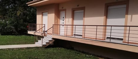 A single-story building with a flat roof, a covered balcony, and a small staircase leading to the entrance.