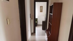 Een gang met een houten bankje, een radiator en een deur naar een andere kamer.