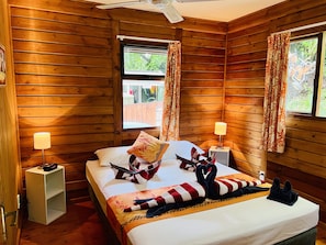 Una habitación de cabaña de madera con una cama, dos lámparas de noche, una ventana con cortinas y un ventilador de techo.