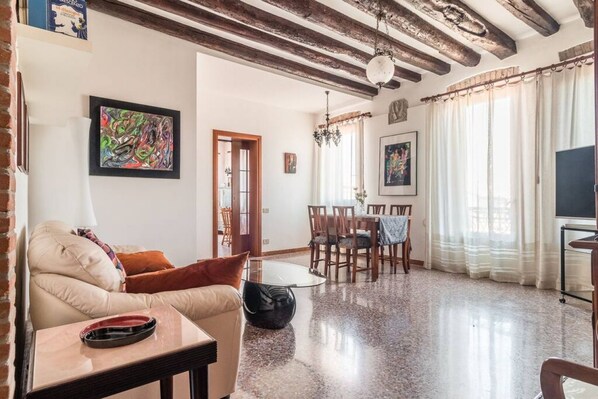 Una sala de estar con un sofá, una mesa de comedor con sillas, un televisor y obras de arte en las paredes.