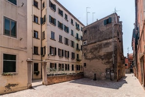 A narrow street with buildings on either side, featuring a mix of architectural styles and a paved ground.