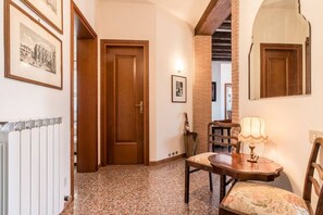 Un couloir avec une porte en bois, un radiateur, une table avec une lampe et des tableaux encadrés accrochés au mur.