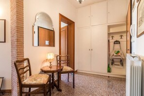 A room with a brick column, a wooden chair with a cushion, a table with a lamp, a white wardrobe, and a radiator. - Colombina House close to @S.Lucia Train Station (Venezia)