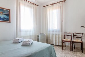 A hotel room with a bed, two chairs, a radiator, and a painting on the wall. - Colombina House close to @S.Lucia Train Station (Venezia)