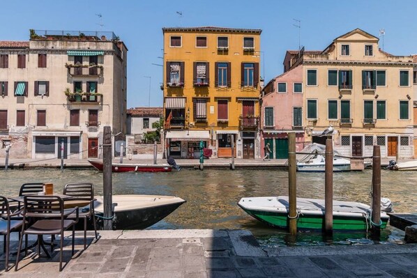 Vista junto a un canal con edificios, barcos y una mesa con sillas.