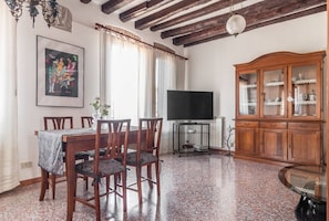 A dining area with a wooden table and chairs, a television on a stand, and a cabinet with glass doors. - Colombina House close to @S.Lucia Train Station (Venezia)