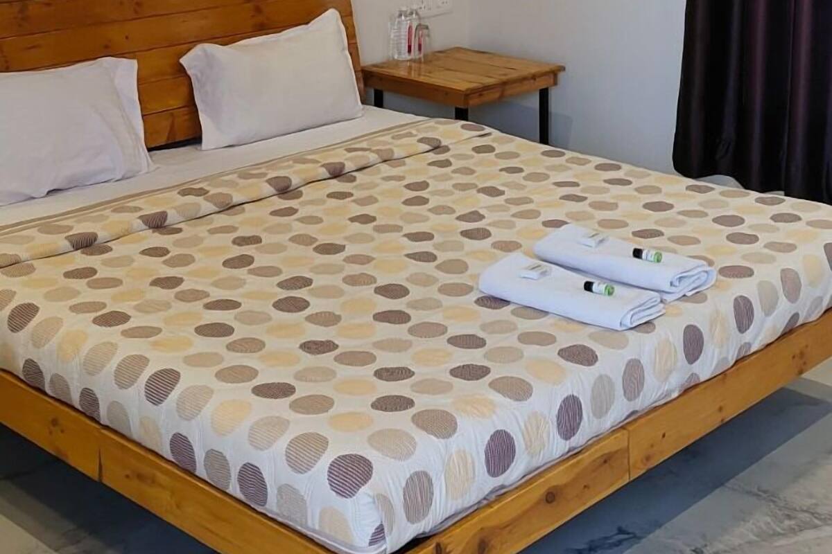 Un dormitorio con cama de madera, ventilador de techo, equipo de aire acondicionado, mesita de noche pequeña y cortina oscura.