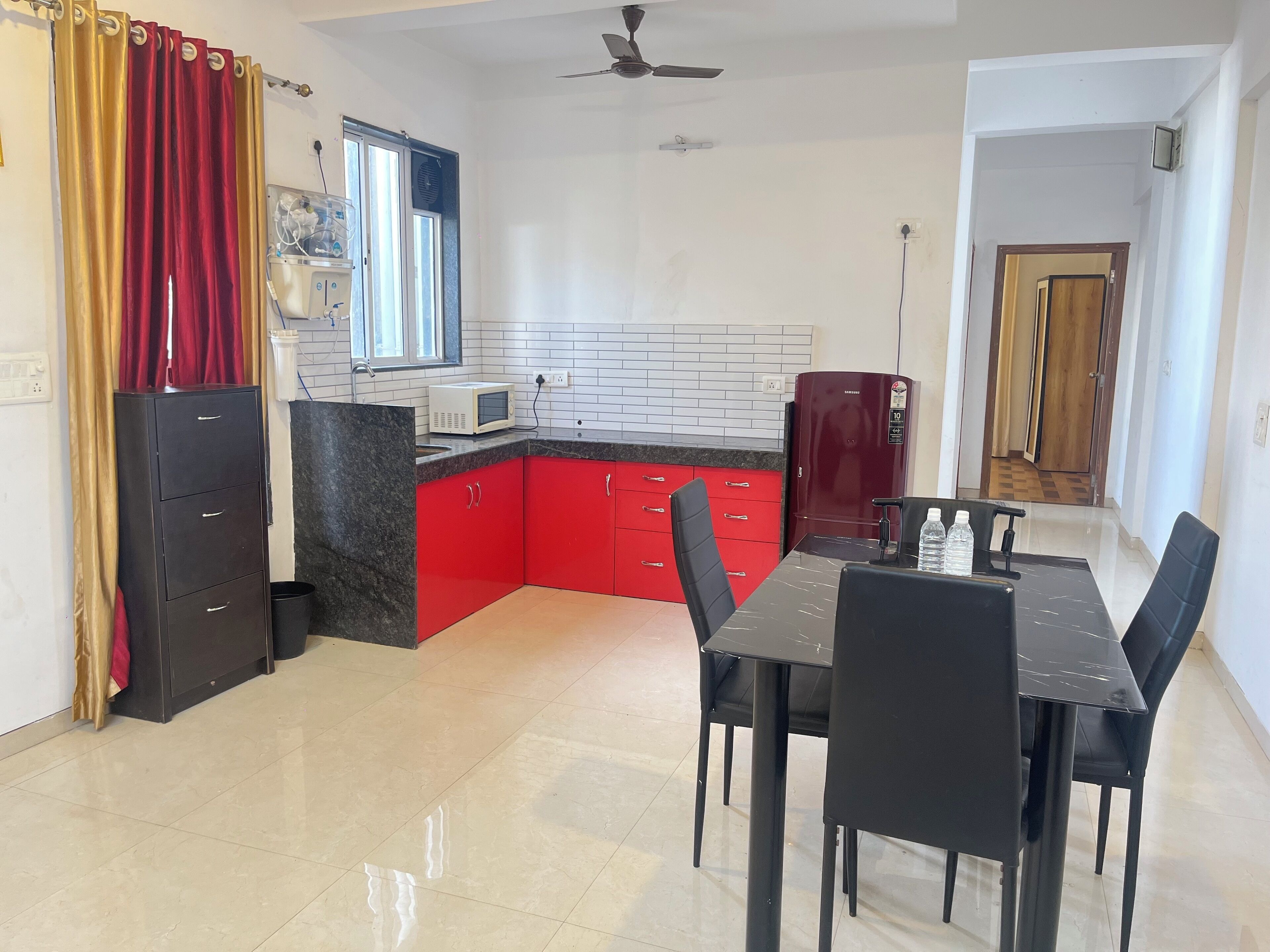 A compact kitchen with red cabinets, a microwave, and a refrigerator. There is a dining table with chairs and a ceiling fan.
