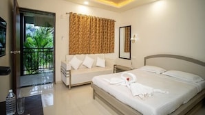 A hotel room with a bed, a sofa, a ceiling fan, a mirror, and a view of a balcony with plants.