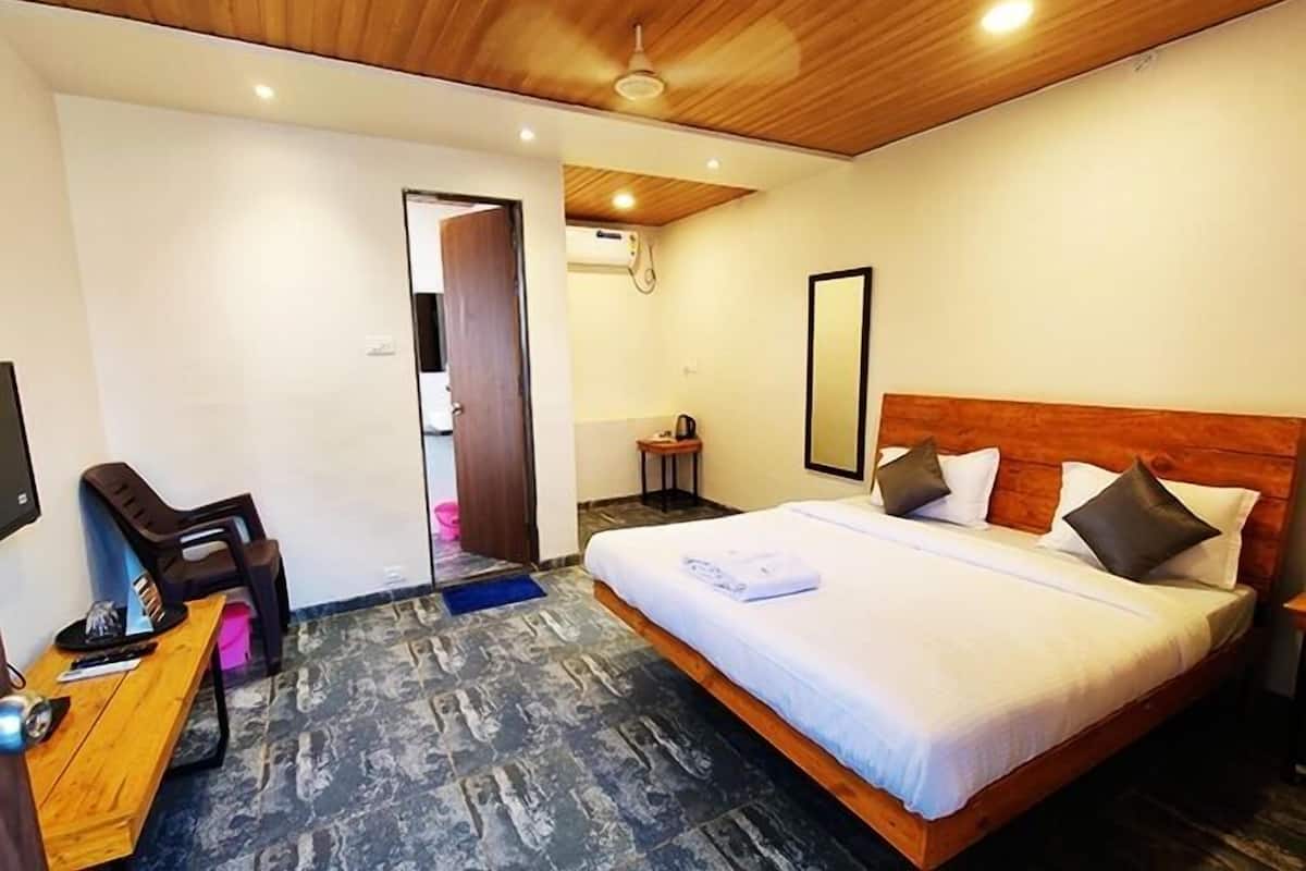 Habitación de hotel con techo de madera, cama con ropa blanca, escritorio con silla y una mesita de noche con lámpara.