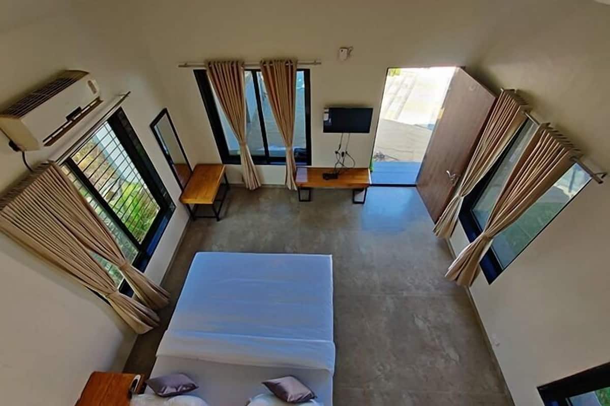 Una habitación con cama, escritorio, televisor y ventanas amplias.