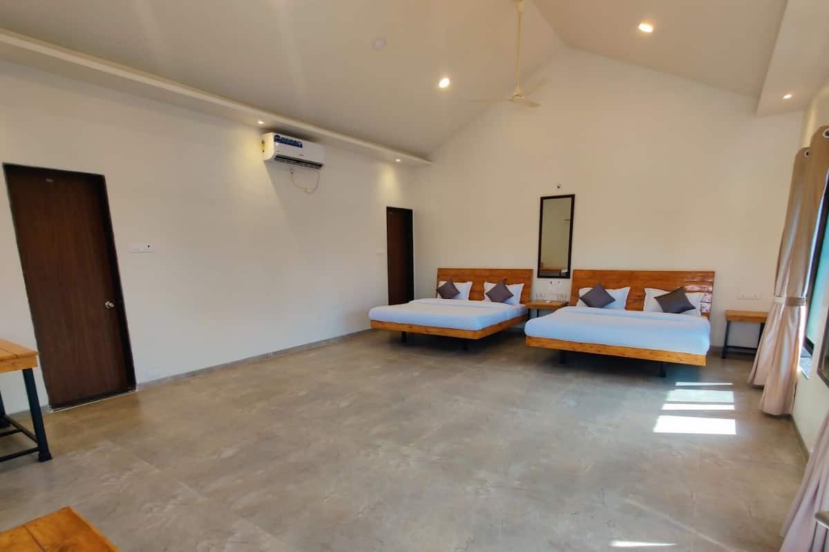 Habitación de hotel con dos camas, ventilador de techo, unidad de aire acondicionado y puerta de madera.