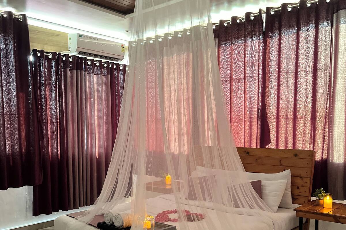 Una cama con dosel, una mesita de noche con una vela y una ventana con cortinas.