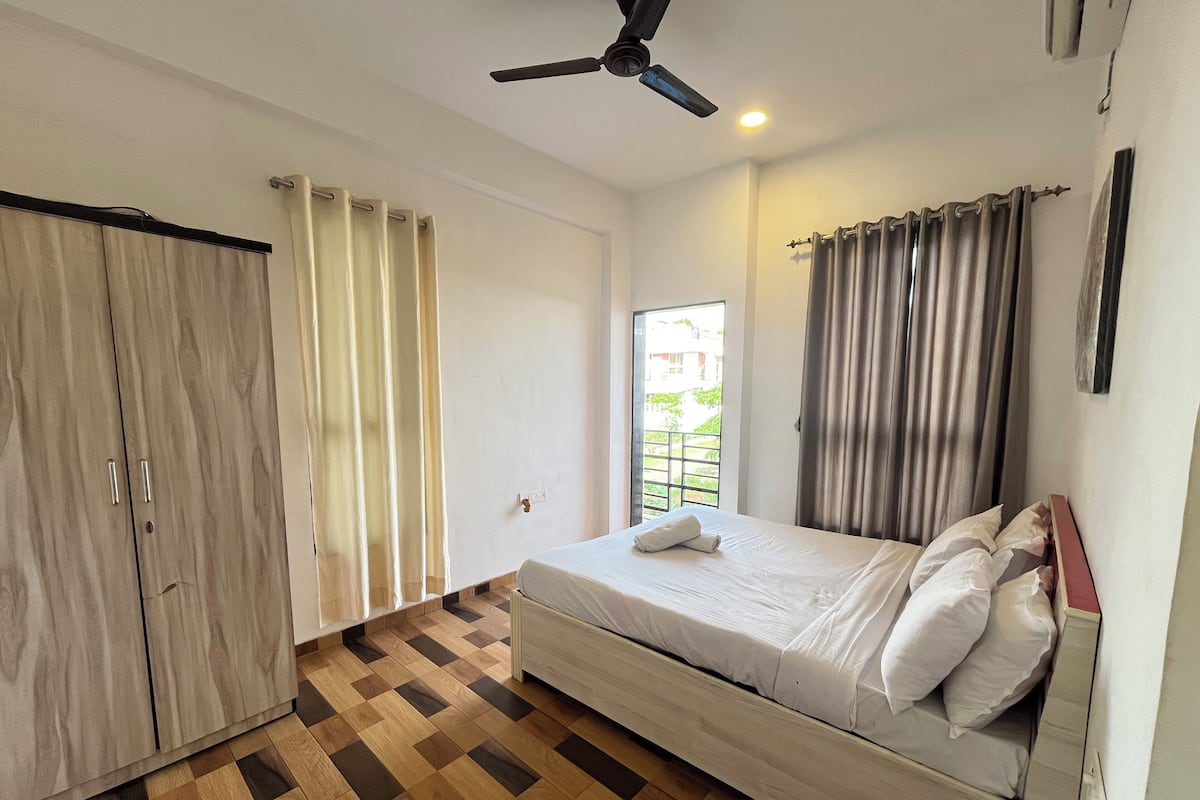 Un dormitorio con cama, armario, ventilador de techo y ventana con cortinas.