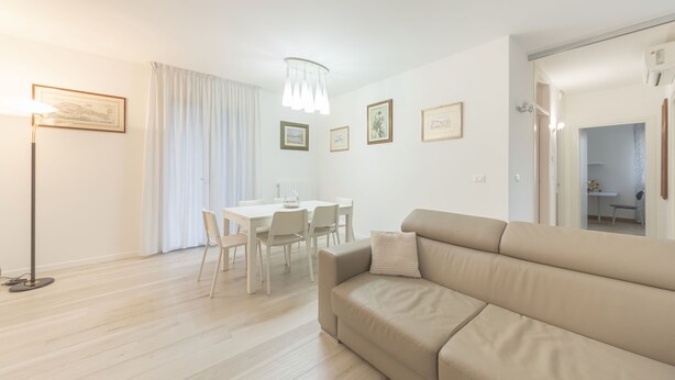 A modern living room with a beige sofa, a dining table with chairs, and a floor lamp. - Da Nonna Antonia (Martellago)