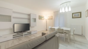 A modern living room with a flat-screen TV, a sofa, a dining table with chairs, and a floor lamp. - Da Nonna Antonia (Martellago)