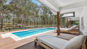 A poolside area with a wooden deck, a lounge chair, and a view of a forest. - HUNTER DREAMING - THE VINTAGE HOLIDAY HOUSES (Pokolbin)