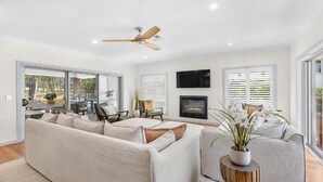 A spacious living room with a large sofa, a fireplace, and a ceiling fan. - HUNTER DREAMING - THE VINTAGE HOLIDAY HOUSES (Pokolbin)