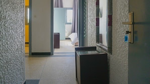 Un couloir avec une porte qui donne sur une pièce. Il y a un miroir sur le mur et une petite table dans la pièce.