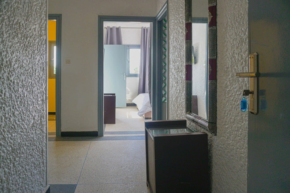 A hallway with a door leading to a room. There is a mirror on the wall and a small table in the room.
