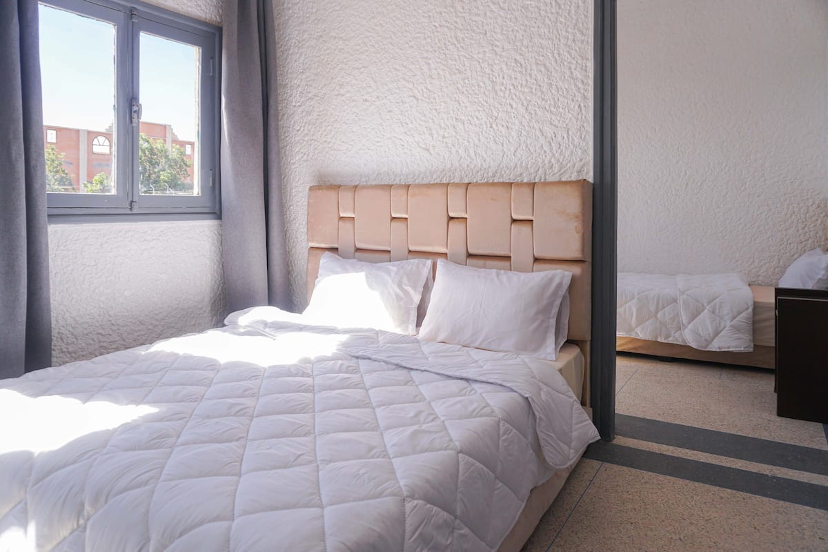 A bedroom with a bed, a window, and a view of buildings outside.