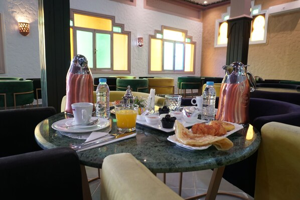 Une table de petit-déjeuner dressée avec une cafetière, des tasses, un verre de jus d’orange et des assiettes remplies de nourriture.