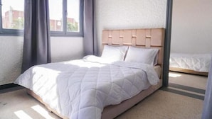 Un lit simple avec une tête de lit en bois, dans une pièce dont le mur est texturé et qui possède une fenêtre.