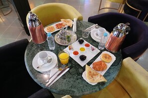 Une table mise pour le petit-déjeuner, avec une nappe, de l’assiette, des couverts, des verres et une variété d’aliments.