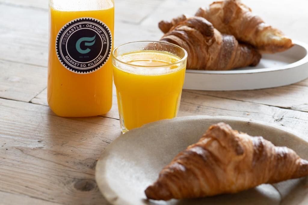 A breakfast setting with a bottle of orange juice, a glass of orange juice, and croissants on a plate.
