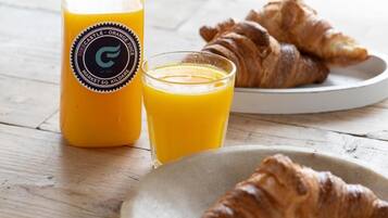A breakfast setting with a bottle of orange juice, a glass of orange juice, and croissants on a plate.