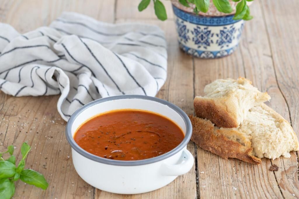 Un tazón de sopa sobre una mesa de madera con un mantel y una planta en maceta al fondo.