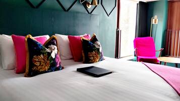 A hotel room with a large bed, multiple pillows, a small table, a chair, and a view of the outdoors.
