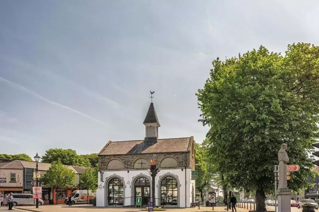 A historic building with a clock tower, arched windows, and a statue in front.