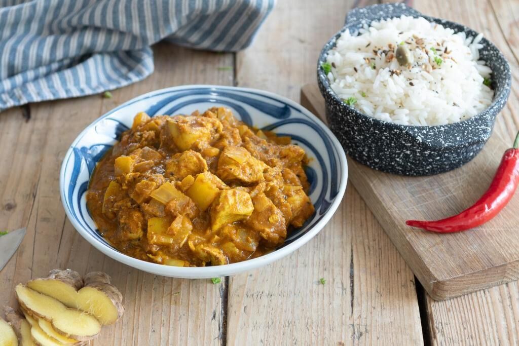 A bowl of curry with rice on a wooden table.