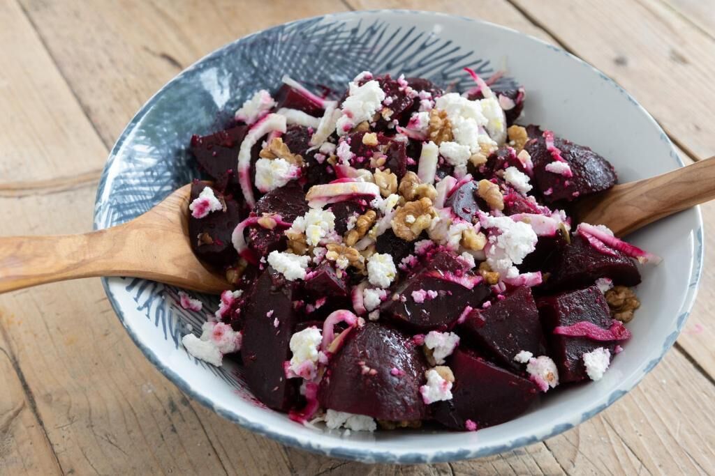 A bowl of beet salad with walnuts and crumbled cheese on a wooden table.